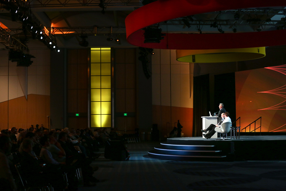 Three men presenting on a dark stage.