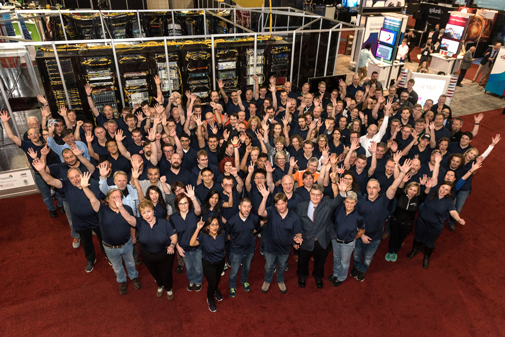 A large group of people smile and put their hands up.